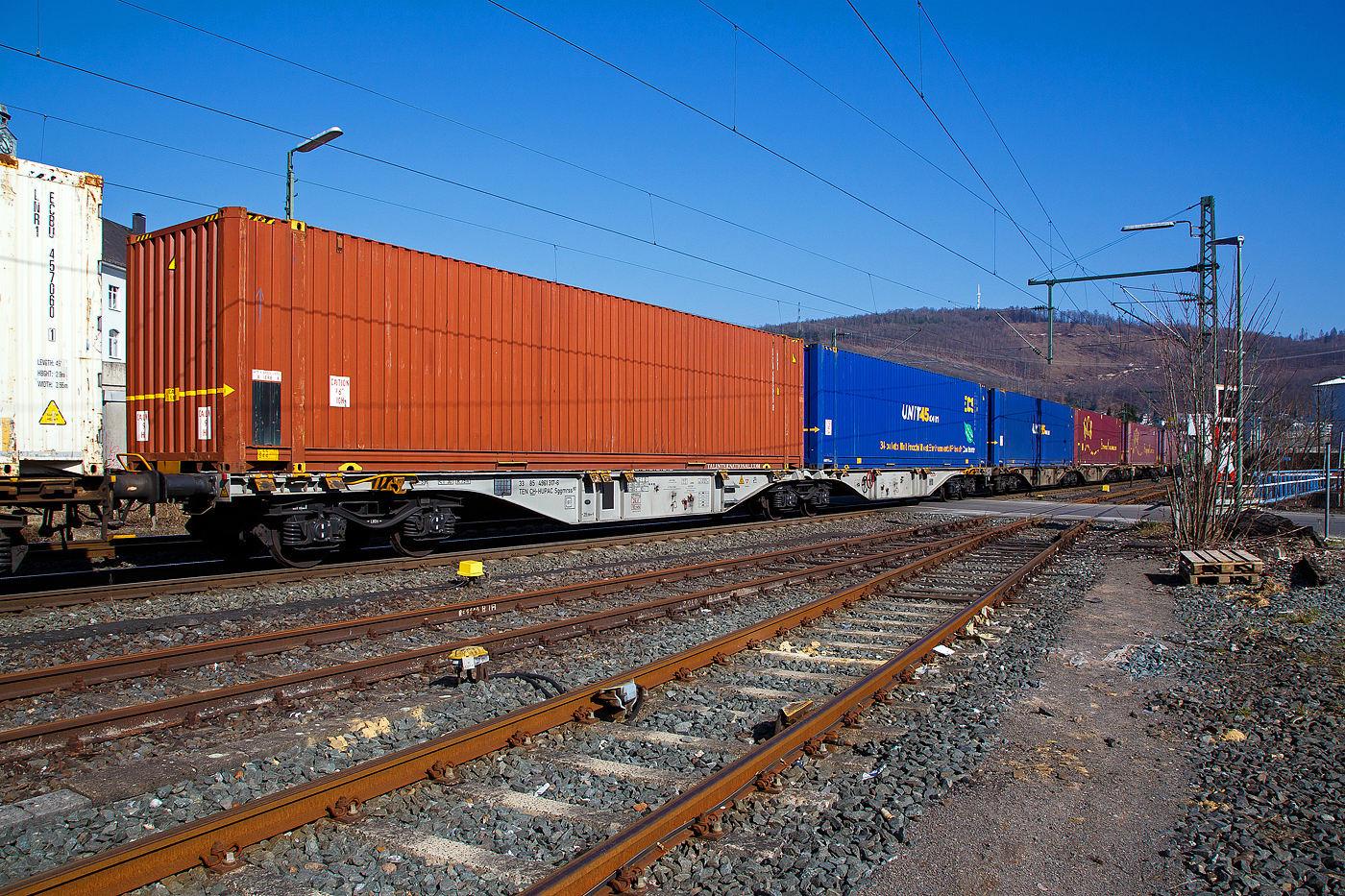 Sechsachsiger Drehgestell-Gelenk-Containertragwageneinheit 90´, 33 85 4961 317-6 CH-HUPAC der Gattung Sggmrss 90`der HUPAC AG am 24.03.2021 im Zugverband bei der Durchfahrt in Niederschelden an der Siegstrecke (KBS 460) in Richtung Siegen.

Diese Gelenkwagen mit sechs Radsätzen sind für den Transport von Großcontainern und Wechselbehältern vorgesehen. Auf den Außenlangträger des Wagens befinden sich für jede vorgesehene Ladeposition feste und klappbare Aufsetzzapfen zum Festlegen der Ladungseinheiten (gemäß UIC- Merkblatt 592-1 und 2) in verschiedenen Kombinationen.

Das aus zwei Wagenhälften bestehende Untergestell ist eine verwindungsweiche, geschweißte Rahmenkonstruktion aus Walz- und Blechprofilen, gebildet aus den Kopfstücken, den Hauptquerträgern und den äußeren Langträgern. In der Wagenmitte befindet sich eine Übersteigmöglichkeit.

TECHNISCHE DATEN:
Spurweite: 1.435 mm
Länge über Puffer: 29.590 mm
Drehzapfenabstand: 2 x 11.995 mm
Achsabstand in den Drehgestellen: 1.800 mm
Drehgestelle: 3 x Y25Lss1-K
Laufraddurchmesser: 920 mm (neu)
Ladelänge: 2 x 13.820 mm
Höhe der Ladeebene über S.O.: 1.155 mm
Eigengewicht: 27.300 kg
Max. Zuladung bei Lastgrenze S: 107,7 t (ab Streckenklasse D)
Max. Zuladung bei Lastgrenze SS: 92,7 t (ab Streckenklasse C)
Max. Geschwindigkeit: 100 km/h (Lastgrenze SS und leer 120 km/h)
Kleinster befahrbarer Gleisbogen: R 75 m 
Bremse: 2 x KE-GP-A 
Bremssohle: Jurid 816M
Feststellbremse: Ja
Verwendungsfähigkeit: TEN GE
