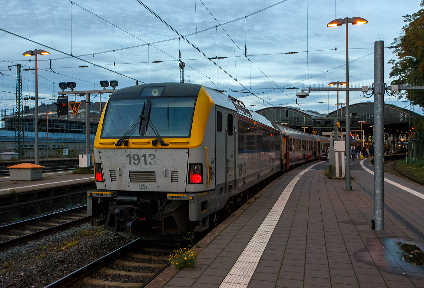 Sie hat uns von Lüttich-Guillemins nach Aachen Hauptbahnhof geschoben, die NMBS/SNCB HLE 1913 hat am frühen Abend des 21 Oktober 2025 mit dem euregioAIXpress - S 41 (S-Zug), von Liège-Saint-Lambert über Welkenraedt den Zielbahnhof Aachen Hbf (französisch d'Aix-la-Chapelle gare centrale) erreicht. Noch kann sie hier einfahren, da auf den Gleisen 6 bis 9 die Netzspannungen der Oberleitungen noch umstellbar ist, dieser Systemwechsel soll jedoch auf die freie Strecke nach Hergenrath verlegt werden. Denn die Loks der NMBS/SNCB-Reihe 18/19: (SIEMENS EuroSprinter ES60U3) sind nur für die Netzspannungen von 25 kV 50 Hz AC, 3 kV DC und 1,5 kV DC vorgesehen. 

Hier kann man auch deutlich den Unterschied zur SNCB/NMBS der Serie/ Reeks 18 sehen, hier die Lokomotiven der Reihe 19 sind einseitig mit automatischen Mittelpufferkupplungen für den Wendezugbetrieb mit M6-Wagen ausgerüstet. Die Loks der Reihe 18 verfügen an beiden Enden über Schraubenkupplungen.
