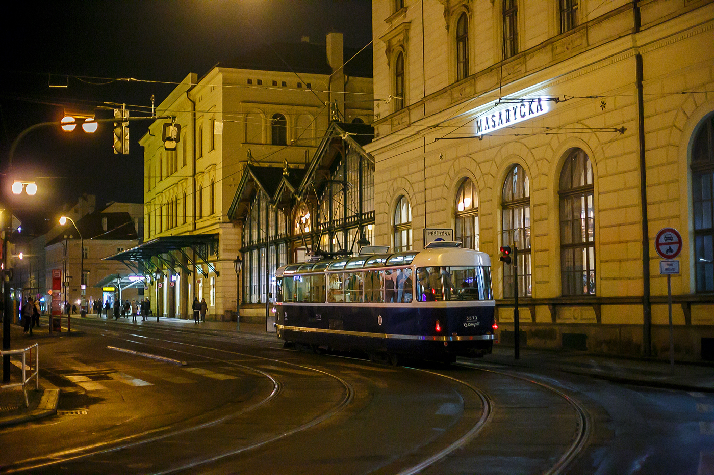 Triebwagen 5573, das T3 Coupé, der Verkehrsgesellschaft der Hauptstadt Prag (DPP - Dopravní podnik hlavního města Prahy a.s.) fährt am Abend des 22.11.2022 über die Havlíčkova beim Bahnhof Praha Masarykovo nádraží vorbei. 

Der Triebwagen vom Typ T3 wurde 1974 von ČKD Tatra in Praha unter der Fabriknummer 162-550 gebaut und als TW 6916 geliefert. In der Prager Hauptwerkstatt UDDP wurde er 2006 zum Typ T3R.P (TW 8497) umgebaut, nach Unfall 2016 wurde er abgestellt. Von CKD Tatra in Praha wurde er 2180 zum Stadtrundfahrtwagen T3 Coupe 5573 umgebaut. So ist er ein Fahrzeug im „Retrodesign“ und kein echter Historischer Wagen.

Praha Masarykovo nádraží ist ein wichtiger Regionalbahnhof und früherer war er auch Fernbahnhof in Prag. Bei diesem Bahnhof befinden auch direkt vor im Straßenbahnhaltestellen (etlicher Linien).
 
Erbaut wurde er in den Jahren 1844/45 im Zuge der k.k. Nördlichen Staatsbahn von Olmütz, welche bis 1851 von Wien nach Dresden durchgehend in Betrieb genommen wurde. Der Bahnhof ist heute der einzige Kopfbahnhof Prags. Er trägt den Namen des ersten Präsidenten der Tschechoslowakei Tomáš Garrigue Masaryk. 

Die ehemaligen Bahnhofsnamen sind:
• 1845–1862 Praha / Prag
• 1862–1919 Praha státní nádraží / Prag Staatsbahnhof
• 1919–1940 Praha Masarykovo nádraží (Prag Masarykbahnhof)
• 1940–1945 Praha Hybernské nádraží / Prag Hibernerbahnhof
• 1945–1952 Praha Masarykovo nádraží
• 1953–1990 Praha střed (Prag Mitte)
• seit März 1990 wieder Praha Masarykovo nádraží
