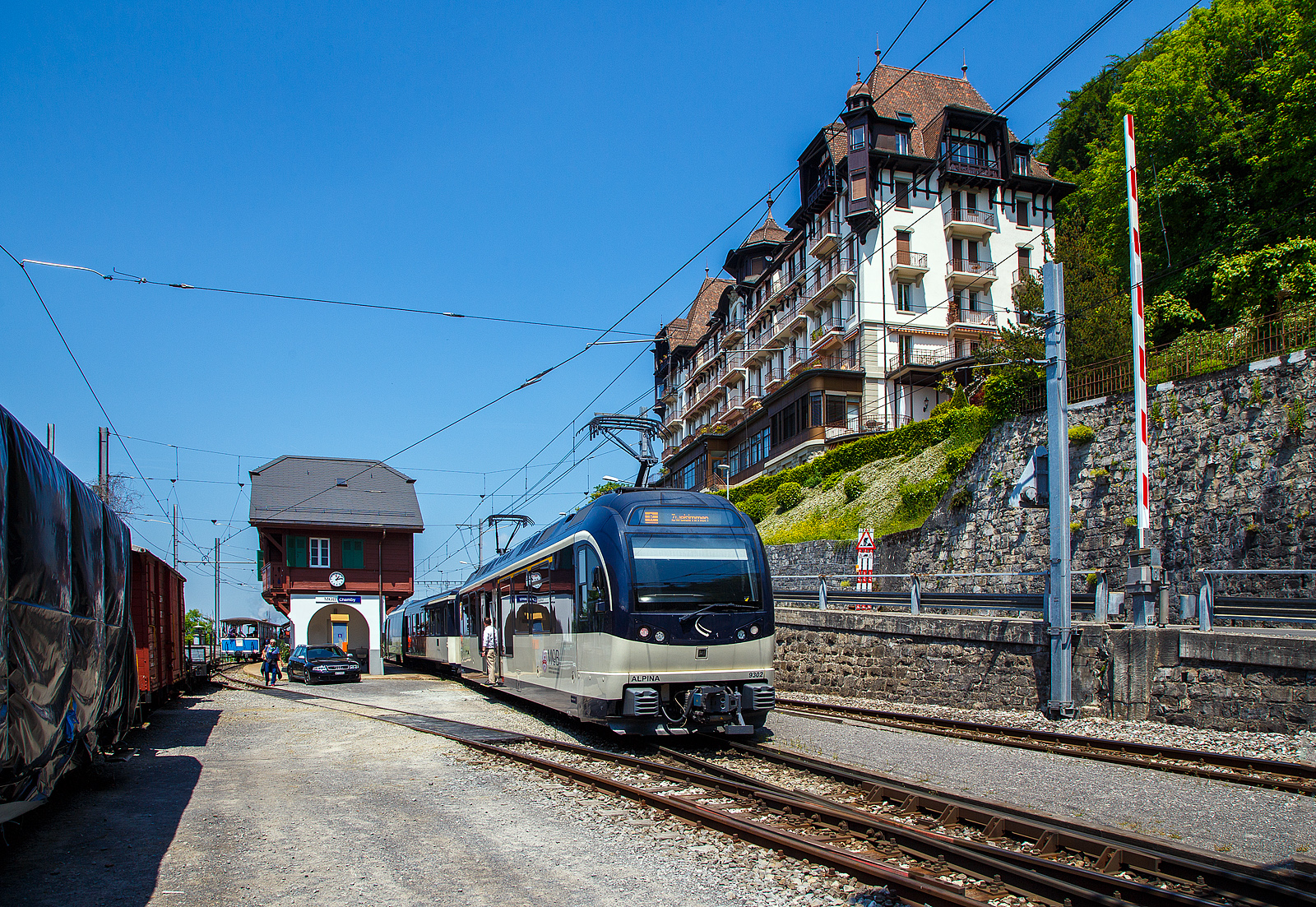 Über dem Genfersee, der Bahnhof Chamby am 27.05.2023.

Der Bahnhof Chamby ist ein Keilbahnhof, und liegt an der MOB (Montreux–Berner Oberland-Bahn) Strecke (KBS 120) Montreux–Montbovon–Zweisimmen, von hier zweigt die Strecke (KBS 115) nach Blonay ab, diese wird in der Sommersaison von der Museumsbahn Blonay–Chamby, gehört aber der Transports Montreux–Vevey–Riviera (MVR, ex CEV). Neben dem Bahnhofsgebäude der MOB befindet sich hier auch ein Ticketschalter der Museumsbahn BC.

Hier im Bild in Blickrichtung Blonay, von links nach rechts, ein Zug der Museumsbahn BC, das MOB Bahnhofsgebäude und MOB Regionalzug (R 2220 von Montreux nach Zweisimmen) am Zugschluss mit dem MOB ALPINA ABe 4/4 9302 „Chateau-d'Oex“. 
