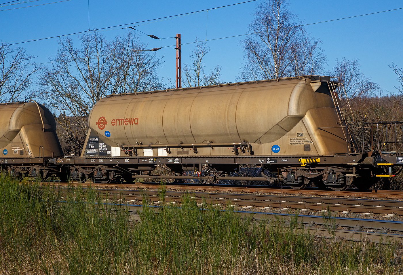 Vierachsiger 80m³ Silowaggon für SO 143 - Aluminiumoxid (Drehgestell-Staubgutwagen) 33 80 9326 673-6 D-ERMD, der Gattung Uacns (Type 6924 B0), französischen Vermietungsfirma ERMEWA S.A., am 07.02.2023 im Zugverband bei einer Zugdurchfahrt bei Wilnsdorf-Rudersdorf.

TECHNISCHE DATEN:
Hersteller: Feldbinder Spezialfahrzeugwerke GmbH, andere Quellen scheiben WB Graaff (1987) als Hersteller, dies kann sich aber nur aufs Fahrgestell beziehen, denn ich kann am Silo deutlich „Feldbinder“ lesen.
Gattung:  Uacns
Spurweite: 1.435 mm
Länge über Puffer : 18.100 mm
Drehzapfenabstand: 13.070 mm
Achsabstand im Drehgestell: 1.800 mm
Höchstgeschwindigkeit: 100 km/h 
Gesamtvolumen: 80 m³ (80.000 l)
Eigengewicht:  18.800 kg
Nutzlast:  71,2t (ab Streckenklasse D)
zul. Gesamtgewicht:  90,00 t
Max. Betriebsdruck: 2,50 bar 
Kleinster bef. Halbmesser:  36 m
Bremse: KE-GP-A (LL)
Bremssohle: IP 116
Intern. Verwendungsfähigkeit: RIV

Die Bedeutung der Gattungs- und Kennbuchstaben (hier Uacs):
U - Sonderwagen 
a - mit vier Radsätzen
c - mit Entladung unter Druck
n – bei mit vier Radsätzen höchste Lastgrenze über 60 t
s - Höchstgeschwindigkeit 100 km/h (beladen)