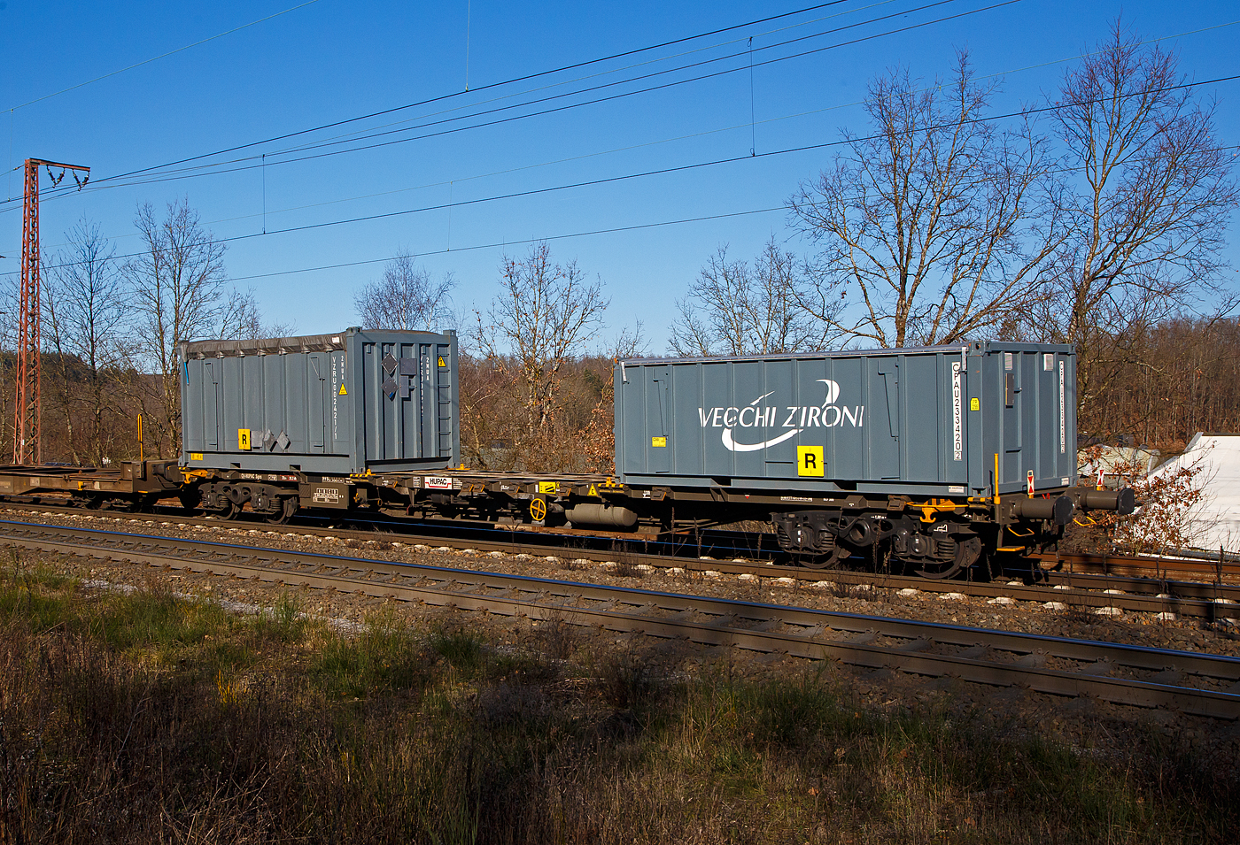 Vierachsiger Drehgestell-Containertragwagen der Gattung Sgns, 33 85 4555 518-8 CH-HUPAC, der HUPAC SA, am 07.02.2023 im Zugverband bei der Durchfahrt in Rudersdorf (Kr. Siegen) in Richtung Siegen.

Bedeutung der Gattung Sgns:
S   Drehgestell-Flachwagen in Sonderbauart
g   Für Container mit einer Gesamtlänge von höchstens 60 Fuß
n   Maximale Tragfähigkeit über 60 t
s   Höchstgeschwindigkeit 100 km/h (beladen)

TECHNISCHE DATEN:
Spurweite: 1.435 mm
Länge über Puffer: 19.640 mm
Drehzapfenabstand: 14.200 mm
Achsabstand in den Drehgestellen: 1.800 mm
Eigengewicht: 20.000 kg
Max. Zuladung: 70,0 t (ab Streckenklasse D)
Max. Geschwindigkeit: 100 km/h (beladen) / 120 km/h (leer)
Kleinster befahrbarer Gleisbogen: R 75 m 
Bremse: Frein 0-GP-A