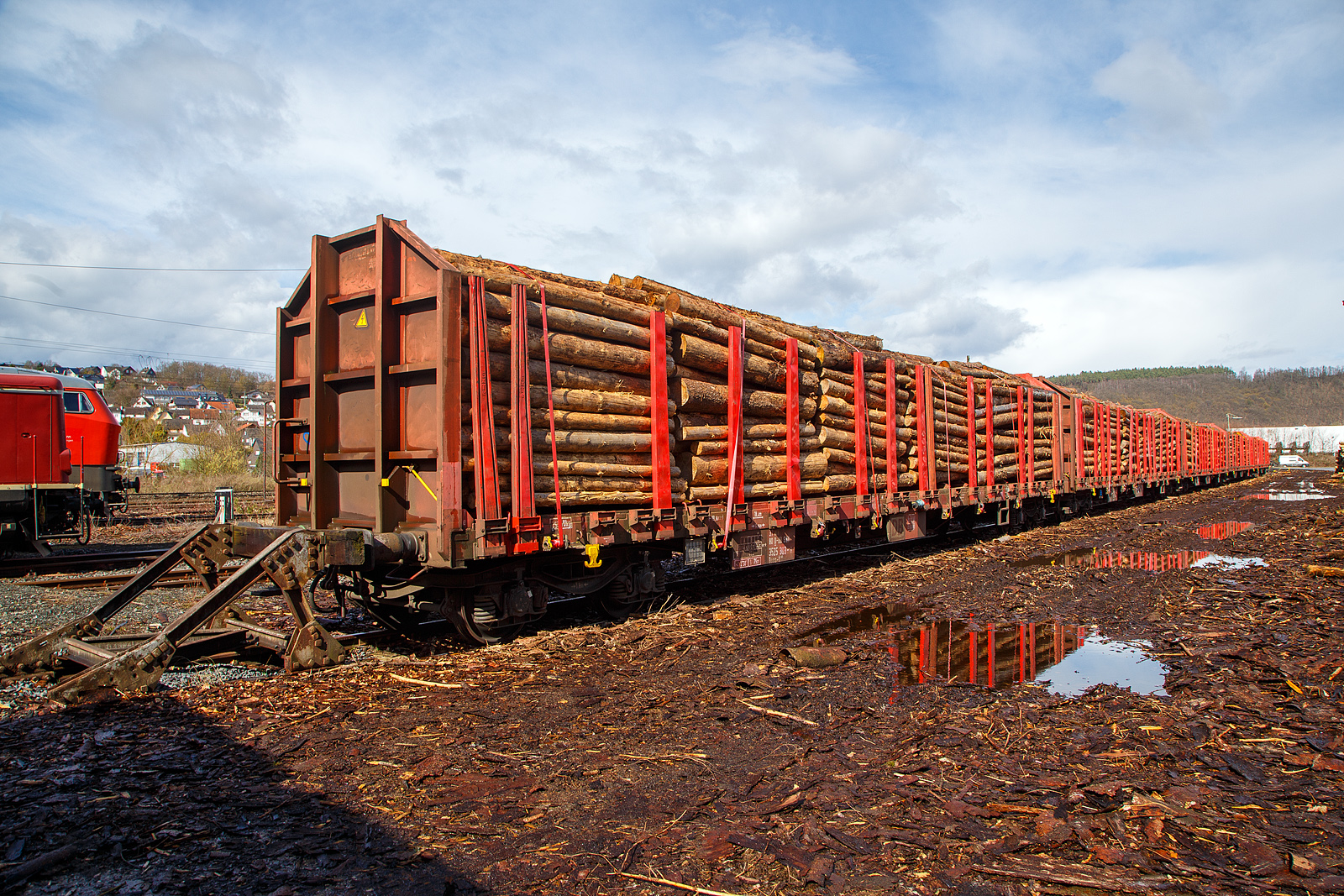 Vierachsiger Drehgestell-Flachwagen für den Holztransport, mit Stirnwänden und Rungen, jedoch ohne Seitenwände, 37 80 3525 303-8 D-DBSNI, der Gattung Roos-t 645, der DB Cargo Logistics GmbH (ex DB Schenker Nieten GmbH), am 25.03.2023 abgestellt beim Kleinbahnhof der WEBA (Westerwaldbahn) in Scheuerfeld (Sieg), hier erfolgt die Verladung vom LKW auf die Wagons. 

Diese Wagen wurden zwischen 2000 und 2003 aus Res 678 bzw. Res 676 Wagen umgebaut. Die Wagen sind speziell für den Transport von langen und schweren Ladegütern vorgesehen - vorrangig für Nadelstammholz, Eichen- und Buchenstammholz sowie Schnittholz. Sie sind mit je nach Holzlänge unterschiedlich positionierbaren Leichtmetallrungen ausgestattet. Am Wagen sind 8 Niederbindeeinrichtungen (Spannwinden mit Gurt 40 kn Nennbruchkraft) und Bindeösen zur Ladungssicherung bzw. für Ladegutabdeckungen vorhanden.

TECHNISCHE DATEN:
Gattung: Roos-t 645
Spurweite: 1.435 mm (Normalspur)
Länge über Puffer: 19.900 mm
Drehzapfenabstand: 14.840 mm
Radsatzstand in den Drehgestellen: 1.800 mm
Ladelänge: 18.400 mm
Ladebreite: 2.650 mm (zwischen den Rungen)
Ladefläche: 48,6 m²
Fußbodenhöhe über SO: 1.380 mm (OK Ladeschwelle)
Rungenhöhe: 1.965 mm
Eigengewicht: 26.300 kg
Zuladung bei Lastgrenze S: 54,5 t (ab Streckenklasse C)
Max. Geschwindigkeit: 100 km/h / 120 km/h (leer)
Kleinster Gleisbogenhalbmesser: 75 m
Bauart der Bremse: KE-GP (LL)
Bremssohle: IB 116
Intern. Verwendungsfähigkeit: RIV
