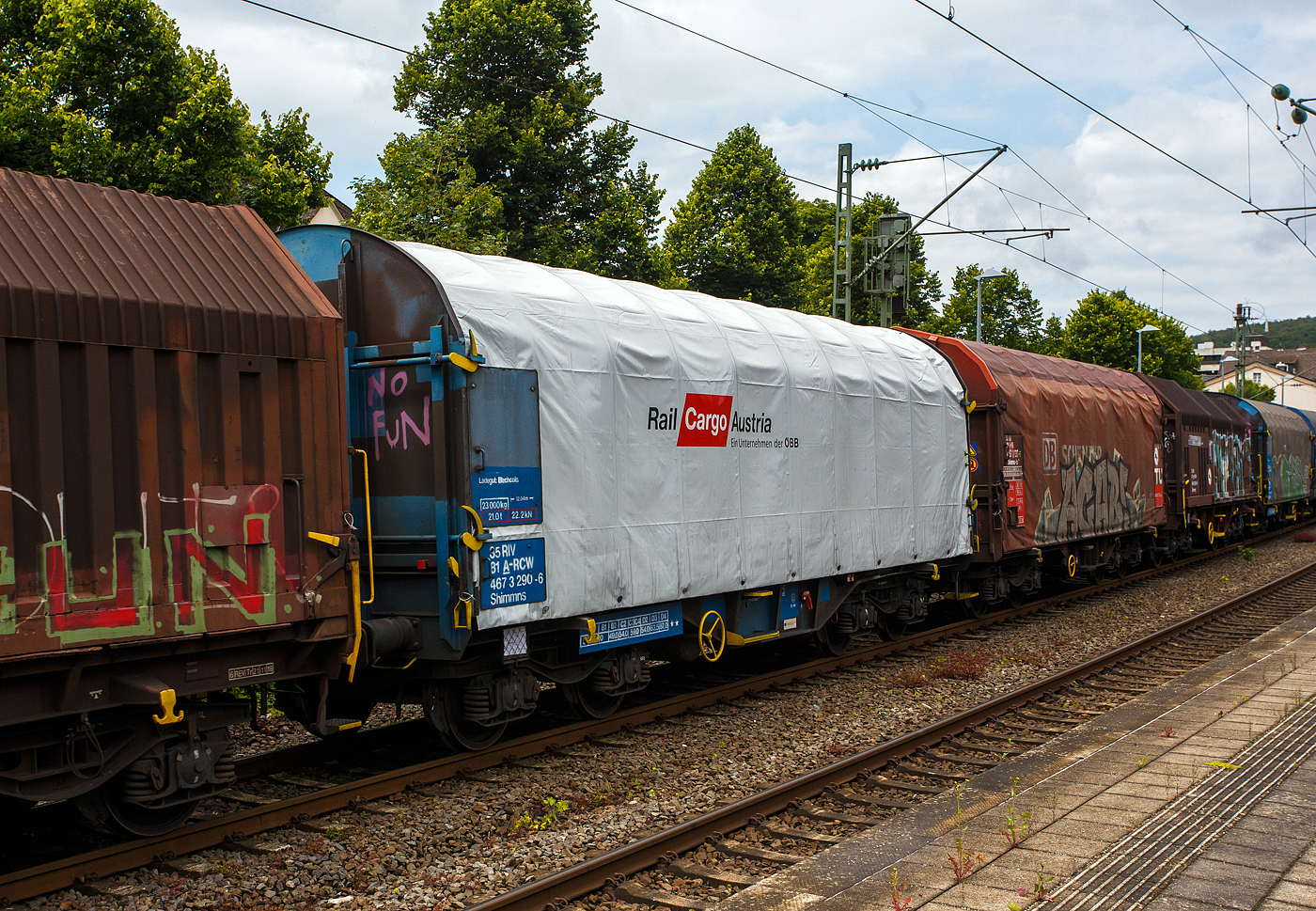 Vierachsiger Drehgestell-Flachwagen mit verschiebbarem Planenverdeck und Lademulden für Coiltransporte, 35 81 4673 290-6 A-RCW, der Gattung Shimmns, der Rail Cargo Austria (ein Unternehmen der ÖBB), am 04 Juli 2024 im Zugverband bei der Zugdurchfahrt im Bahnhof Kirchen(Sieg).

TECHNISCHE DATEN:
Spurweite: 1.435 mm
Achsanzahl: 4 (in 2 Drehgestelle)
Länge über Puffer: 12.040 mm
Länge der Ladefläche: 10.800 mm
Drehzapfenabstand: 7.000 mm
Achsabstand im Drehgestell: 1.800 mm
Eigengewicht: 23.000 kg
Höchstgeschwindigkeit: 100 km/h (beladen) / 120 km/h (leer)
Maximales Ladegewicht: 67,0 t (ab Streckenklasse D4)
Mulden: 5 Stück, im Untergestell integriert
Bauart der Bremse: KE-GP-A (LL)
Bremssohle: IB116
Intern. Verwendungsfähigkeit: RIV
