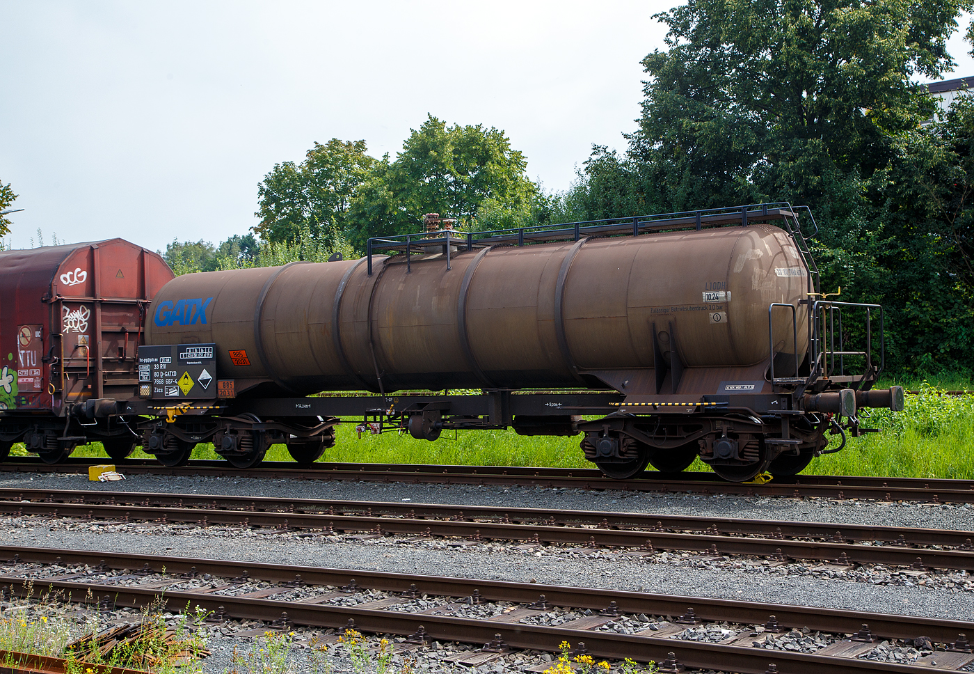 Vierachsiger-Drehgestell Kesselwagen für Salpetersäure (>97%), der Gattung Zacs, registriert als 33 80 7868 687-4 D-GATXD der GATX Rail Germany GmbH abgestellt am 24.08.2023 auf dem Rbf der KSW in Herdorf, im Zugverband eines Übergabezuges der KSW.

Die Gefahrguttafel (885/2031) zeigt es auch noch an: (oben) Gefahrgutnummer 885 = stark ätzender Stoff / (unten) UN-Nummer 2031 = Salpetersäure, andere als rotrauchend, mit mehr als 70 % Säurebrandfördernd. Hier sogar (laut Anschrift) größer 97 %. Die reine Säure ist farblos und hat einen scharf stechenden Geruch. Sie wird unteranderem zur Herstellung von Sprengstoffen verwendet, was hier der Fall ist.

TECHNISCHE DATEN:
Gattung: Zacs
Spurweite: 1.435 mm
Länge über Puffer : 14.240 mm
Drehzapfenabstand: 9.200 mm
Achsabstand im Drehgestell: 1.800 mm
Höchstgeschwindigkeit: 100 km/h (120 km/h leer)
Eigengewicht: 20.985kg
Nutzlast: 59,0t ab Streckenklasse C
Gesamtvolumen: 44.900 Liter
Prüfdruck: 4 bar
Zulässiger Betriebsüberdruck: 3 bar
Tankcode: L10DH
Behälterwerkstoff : Edelstahl
Bremse: KG-GP
Intern. Verwendungsfähigkeit: RIV
