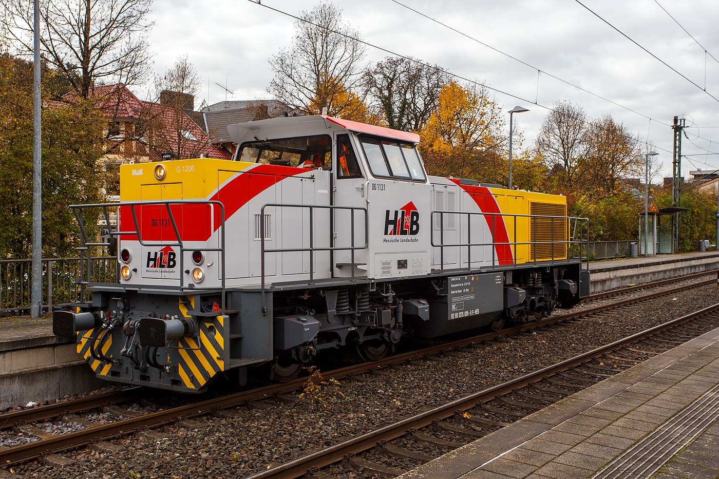 Welch seltener Gast auf der Siegstecke, auch wenn Triebzüge und -wagen der HLB hier Alltag sind, ist die Güterlok der HLB meist in und um Kassel unterwegs. Die Diesellokomotive 275 024-8, alias DG 1131 (92 80 1275 024-8 D-HEB), die Vossloh/MaK G 1206 der HLB - Hessische Landesbahn GmbH, hat am 16 Oktober 2025, auf den Weg in Richtung Köln, im Bahnhof Kirchen/Sieg Hp 0, da es eine Weichenstörung gab.

Die MaK G 1206 wurde 2001 von der VSFT - Vossloh Schienenfahrzeugtechnik GmbH in Kiel-Friedrichsort unter der Fabriknummer 1001131 gebaut und an die LC - Locomotion Capital Ltd. (London) als Mietlok geliefert. 

Lebenslauf/Stationen und Bezeichnungen:
•	Dezember 2001 - Vermietung an NE - Städtische Hafenbetriebe Neuss
•	Januar 2002 - Vermietung an StEK - Städtische Eisenbahn Krefeld 
•	Januar 2002 - Vermietung an Niederrheinische Verkehrsbetriebe AG (NIAG) 
•	Januar/Februar 2002 - Vermietung an OHE- Osthavelländische Eisenbahn AG 
•	Februar 2002 bis August 2003 - Vermietung an IL - InfraLeuna Infrastruktur- und Service GmbH, als IL 206
•	April 2003 - Verkauf an ATC - Angel Trains Cargo SA, Antwerpen (B)
•	August 2003 bis - Vermietung an RBH - RAG Bahn und Hafen GmbH als  RBH 841  
•	April bis Juni 2005 - Vermietung an MEG - Mitteldeutsche Eisenbahn GmbH  MEG 298  
•	November 2005 bis Oktober 2006 - Vermietung an MVG - Mülheimer Verkehrsgesellschaft mbH, Mülheim (Ruhr)  2  
•	November 2006 bis 2013 Vermietung an CFL - Société Nationale des Chemins de Fer Luxembourgeois bzw. CFL Cargo als 1504. Ab 2007 dann NVR-Nummer 92 82 0001 504-0 L-CFLCA. Zum 01.01.2010 aus der ATC wird die Alpha Trains Belgium NV/SA. 
•	Juni 2013 bis Dezember 2014 - Vermietung an HLB - Hessische Landesbahn GmbH  
•	31.12.2014 - Verkauf an die HLB - Hessische Landesbahn GmbH, Betreiber Bezeichnung  DG 1131 , vergabe der NVR-Nummer 92 80 1275 024-8 D-HEB. Auffällig ist das sie, trotz der längeren Einsatzdauer in Luxemburg, heute nur die UIC-Zulassung für Deutschland (D) hat. 

Die MaK G 1206 ist im schweren Rangier- und Streckendienst einsetzbar. Sie wurde 1997 zum ersten Mal gebaut und ist nach Deutschland, Österreich, der Schweiz, Luxemburg, Italien, Spanien, den Niederlanden und nach Frankreich verkauft worden. Allein 23 Lokomotiven fahren als BB 61000 bei der SNCF, davon sechs mit MTU-Motor (Die G 1206 gibt es wahlweise mit Caterpillar- oder MTU-Motor). Diese Lok hat einen Caterpillar 12 Zylinder 4-Takt Dieselmotor mit Abgasturbolader und Ladeluftkühlung vom Typ 3512B DI TA-SC mit einer Leistung von 1.500 kW bei1.800 U/min. Das Strömungsgetriebe ist ein Voith L 5r4 zU2.
