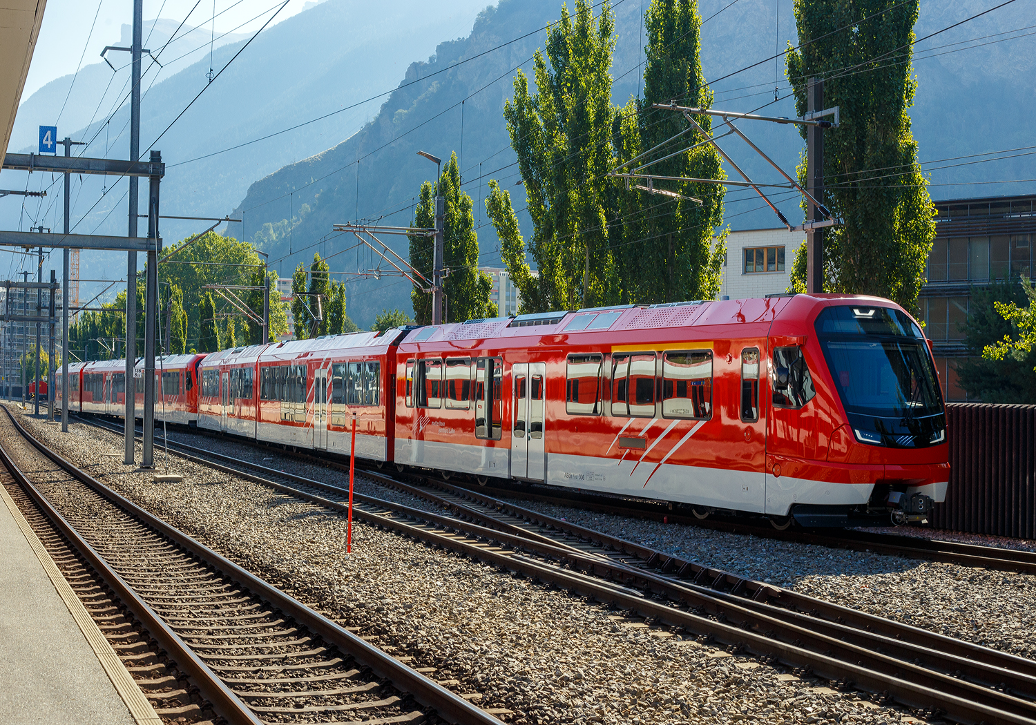 Zwei gekuppelte dreiteilige sehr neue MGB ABeh 8/12 „ORION“ Niederflurtriebz�ge mit Zahnrad- und Adh�sionsantrieb erreichen am 11 September 2023, als MGB R 43 (525) von Andermatt nach Visp, ihr Ziel den Bahnhof Visp. Vorne der MGB ABeh 8/12 306 und dahinter der 305 „Gornergrat“.

Die ABeh 8/12 „ORION“ sind die neusten Triebz�ge der MGB – Matterhorn Gotthard Bahn, der erste wurde von Stadler am 12. September 2022 an die MGB ausgeliefert. Am 15. Juni 2023 fand auf dem Oberalppass das offizielle Roll-In der ORION-Z�ge statt, sechs Triebz�ge wurden in den kommerziellen Betrieb �bernommen. Die Typbezeichnung ORION steht f�r �Optimaler Regionalzug Im Oeffentlichen Nahverkehr�. Mit den neuen Triebz�gen werden leider �ltere Lokomotiven samt den dazugeh�rigen Personenwagen im Regionalverkehr ersetzt. Ab Ende 2023 sollen dann alle zw�lf Triebz�ge im regul�ren Fahrplan unterwegs sein. In einer zweiten Etappe ist die Anschaffung von mindestens 25 dreiteiligen Triebz�gen mit gemischtem Adh�sions- und Zahnradantrieb bis 2028 geplant, zudem vier Einheiten mit reinem Adh�sionsantrieb. Das Investitionsvolumen betr�gt �ber 400 Millionen Franken. Bis zum September 2023 wurden 12 Z�ge (301 bis 312) ausgeliefert und in Betrieb genommen.

Die neuen �ORION� - Z�ge zeichnen sich durch eine besondere Kundenfreundlichkeit und ihre hohe Flexibilit�t aus. Von den durchg�ngigen Niederflureinstiegen mit ebenerdigem Ein- und Ausstieg profitieren Rollstuhlfahrer, Familien mit Kinderwagen und Senioren gleicherma�en. Dazu verf�gt jeder Wagen �ber ein Multifunktionsabteil zum Verstauen von Gep�ck und Sportger�ten. Zudem sind die neuen Z�ge mit einem WLAN-Zugang ausger�stet.

Aus betrieblicher Sicht bieten die Z�ge flexible Einsatzm�glichkeiten. Sie sind auf dem gesamten Streckennetz der MGB zwischen Zermatt bis Disentis einsetzbar und k�nnen auch die maximale Steigung von 181‰ zwischen G�schenen und Andermatt �berwinden. Die neuen Triebz�ge k�nnen zudem in Doppel- oder Dreifachtraktion verkehren. Sie bieten damit bis zu 990 Fahrg�sten Platz und verf�gen �ber bis zu 444 Sitzpl�tze, davon 66 in der ersten Klasse.
 
Neben dem konsequenten Einsatz von Leichtbaumaterialien zeichnen sich die ORION durch energieeffiziente Antriebskomponenten der neusten Generation, eine Energieoptimierung im Schlummerbetrieb sowie einen niedrigen Energieverbrauch aufgrund �lfreier Trockentransformatoren aus.

Urspr�nglich wollte die MGB Fahrzeuge auf der Basis der FINK-Triebz�ge der zb -Zentralbahn beschaffen. Das war aber aus mehreren Gr�nden nicht m�glich:
 • Die Achslast der Fink-Z�ge betr�gt knapp 17 Tonnen, bei der MGB sind aber nur 16 Tonnen zul�ssig.
 • F�r den Winterbetrieb auf dem Oberalppass ist ein gr�sserer Schneer�umer notwendig.
 • F�r die 179 ‰ steile Sch�llenenbahn h�tte der �Fink� zu wenig Zahnrad-Drehgestelle.

Die beiden Endwagen der Orion-Triebz�ge haben je zwei gleich konzipierte Antriebsdrehgestelle mit einem Zahnrad- und einem Adh�sionsantrieb. Der Mittelwagen ist mit zwei Bremsdrehgestellen versehen. Die Anordnung der Traktionsausr�stung f�hrt zu einem m�glichst gro�en Gewicht der Endtriebwagen, womit bei starkem Schneefall die Entgleisungssicherheit auf dem Oberalppass verbessert wird. Diese Konzept�nderung f�hrte zu einem um etwa 15 Prozent h�heren Beschaffungspreis als urspr�nglich erwartet. Ein dreiteiliger Zug wird nun fast 12,4 Millionen Franken kosten. Die neuen Fahrzeuge werden gegen�ber den Komet-Z�gen �ber einen zweiten Stromabnehmer, �ber Schiebetritte statt Klapptritte und �ber erweiterte Multifunktionsabteile verf�gen. Die Triebz�ge sind kompatibel f�rs RhB-Netz zwischen Disentis und Landquart.

Zur Abl�sung der Pendelz�ge mit den Deh 4/4 21–24 der ehemaligen BVZ, der vier nicht modernisierten HGe 4/4 II und der �ltesten Reisezugwagen ben�tigt die Matterhorn-Gotthard-Bahn 12 neue Triebz�ge.

Die 15 Garnituren der zweiten Beschaffung werden bis 2029 die ehemaligen FO-Gep�cktriebwagen Deh 4/4 51–55 und Deh 4/4 91–96 ersetzen. Vier Z�ge der zweiten Serie sollen als reine Adh�sionsfahrzeuge f�r den Pendelverkehr zwischen T�sch und Zermatt beschafft werden. Der im Rahmen des Bahnausbauschritts 2035 geplante Tunnel �Unnerchriz� soll den Zahnstangenabschnitt T�schsand–Kalter Boden abl�sen.

TECHNISCHE DATEN der ORION:
Typenbezeichnung: ABeh 8/12 (8 von 12 Achsen angetrieben)
Einsatzgebiet: Zermatt – Disentis / Andermatt – G�schenen / Disentis – Landquart
Nummerierung (2013): 301 - 312 
Spurweite: 1.000 mm (Meterspur)
Zahnradsystem: 	Abt
Achsfolge: Bo'zz Bo'zz + 2' 2' + Bo'zz Bo'zz
L�nge �ber Kupplung: 56. 600 mm
H�he: 3.885 mm
Breite: 2.650 mm
Achsabstand im Trieb-Drehgestell: 2.400 mm 
Achsabstand im Laufdrehgestell: 1.900 mm
Treib- und Laufraddurchmesser: 790 mm (neu)
Eigengewicht: 114 t
Max. Dienstgewicht: 139 t
H�chstgeschwindigkeit (Adh�sion): 120 km/h 
H�chstgeschwindigkeit (Zahnstange): 35 km/h bergw�rts
Dauerleistung am Rad: 1.160 kW (Adh�sion) / 1.600 kW (Zahnrad)
Max. Leistung am Rad: 1.600 kW (Adh�sion)  / 2.400 kW (Zahnrad)
Anfahrzugskraft: 320 kN
Anfahrbeschleunigung:  0.8 m/s�
Stromsystem: 11500 V, 16.7 Hz ~ (AC)
Sitzpl�tze: 24 in der 1. Klasse / 122 in der 2. Klasse, davon 32 Klappsitze 
Stehpl�tze 209
Fu�bodenh�he: 435 mm (Niederflur) / 1.050 mm (Hochflur)
T�ren je Seite: 3
Einstiegbreite: 1.400 m

Bemerkung: F�r die Kompensation vom Radverschlei� besitzen die Z�ge h�henverstellbare Zahnradantriebe.

Quellen: MGB, Stadler Rail und Wikipedia
