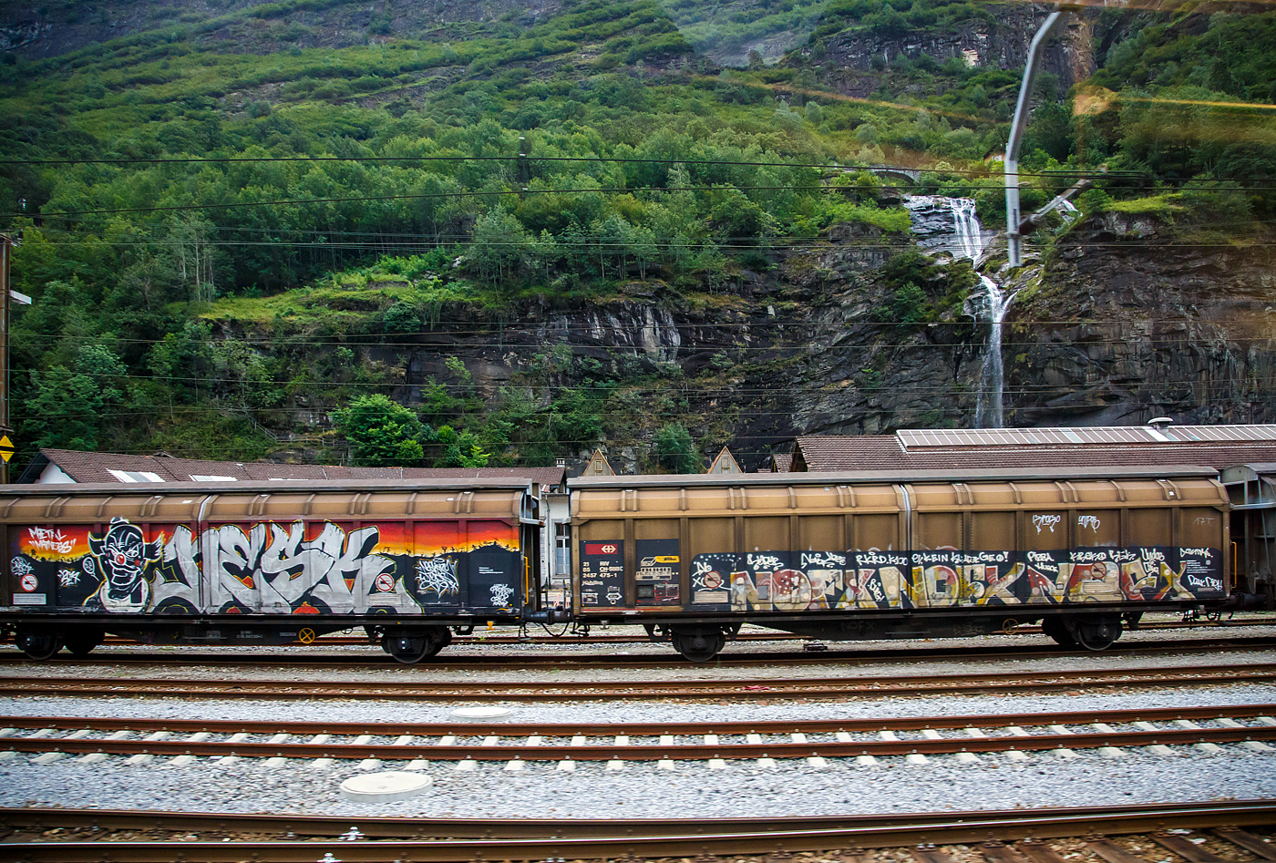 Zweiachsiger, großräumiger Schiebewandwagen 21 85 2457 475-1 CH-SBBC, der Gattung Hbbillns, der SBB Cargo AG, abgestellt am 02 August 2025 in Airolo. Das Bild entstand aus einem Zug heraus.

Der Güterwagen ist ein gedeckter zweiachsiger Schiebewandwagen mit fest verriegelbaren Trennwänden. Speziell geeignet für empfindliche Güter auf Paletten. Schützt vor Nässe und Transporteinwirkungen.

Die Be- und Entladung erfolgt seitlich, ca. die ½ Seite lässt sich öffnen. Das max. Ladegewicht beträgt 28,5 t (38 Paletten)

TECHNISCHE DATEN:
Spurweite: 1.435 mm
Länge über Puffer: 16.720 mm
Achsabstand: 10.000 mm
Länge x Breite der Ladefläche: 13.700 x 2.900 mm
Eigengewicht: 19.500 kg
Ladefläche: 39,7 m²
Rauminhalt: 99,4 m³
Max. Ladegewicht: 21,0 t (ab Streckenklasse C) / 28,5 t (ab Streckenklasse D)
Höchstgeschwindigkeit: 100 km/h (beladen) / 120 km/h (leer)
Bremse: KE-GP-A (K)
Bremssohle: Jurid 816M
Feststellbremse: Nein
Kleinster, befahrbarer Gleisradius: R 35 m
Intern. Verwendungsfähigkeit: RIV

Die Bedeutung der Gattungs- und Kennbuchstaben (hier Hbbillns):
H - Gedeckter Wagen in Sonderbauart
bb - Ladelänge 14 m und mehr
i - Schiebewände
ll - Verriegelbare/bewegliche Trennwände
s - Höchstgeschwindigkeit 100 km/h (beladen)

