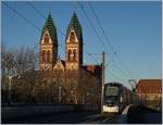 Vor dem Hintergrund der Kath. Kirche  Herz-Jesus  in Freiburg im Breisgau erreicht eine Strassenbahn in K�rze die Haltestelle Hauptbahnhof.

29. Nov. 2016
