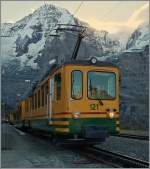 Weiterhin mit einem Stück  fehlender  Fahrleitung, nun aber farblich verändert, präsentiert sich der WAB BDeh 4/4 121 vor dem Mönch beim Halt auf der noch schattigen Wengern Alp.